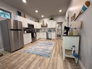 A modern kitchen with stainless steel appliances, white cabinetry, and a blue patterned rug.