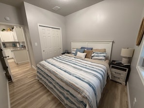A bedroom with a bed, bedside tables, a nightstand, a lamp, and a door to a bathroom.