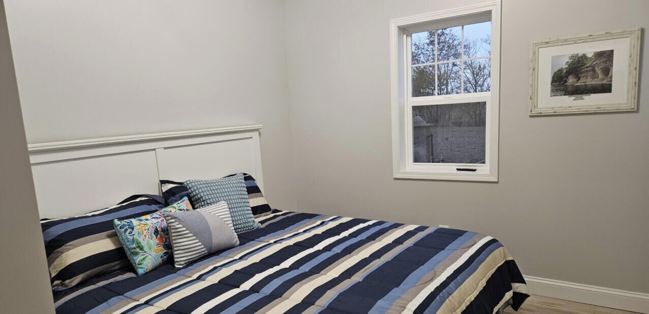 Une chambre à coucher avec un lit, des oreillers, une fenêtre et un tableau encadré au mur.