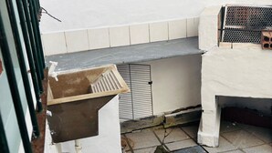 A rooftop terrace with a white wall, a metal grill, and a white table.