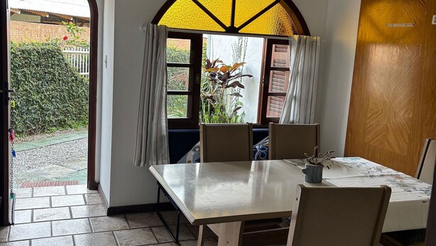 A dining area with a table and chairs, a view through a window, and a door leading outside.