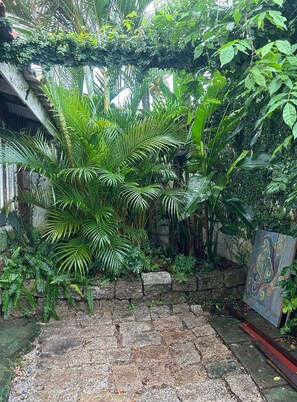 A garden with a stone pathway leading to a door, surrounded by lush greenery and plants.