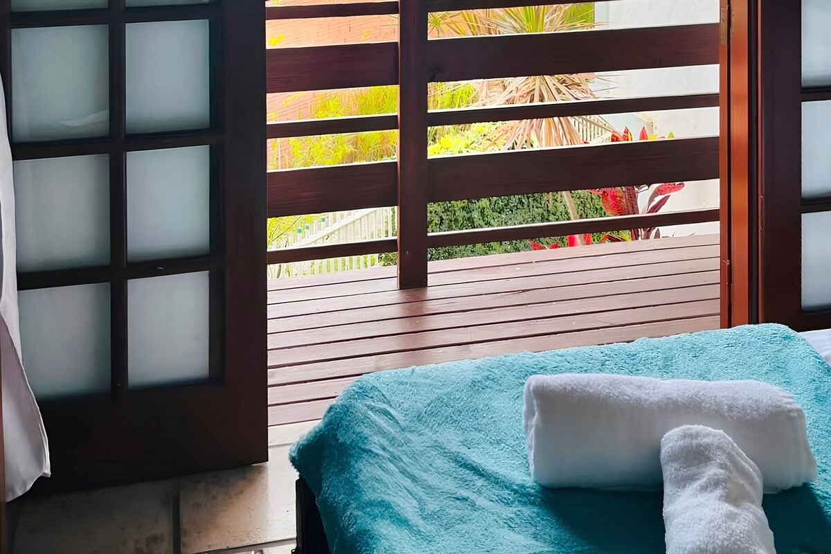 A room with a bed, a wooden railing, and a view of a residential area.