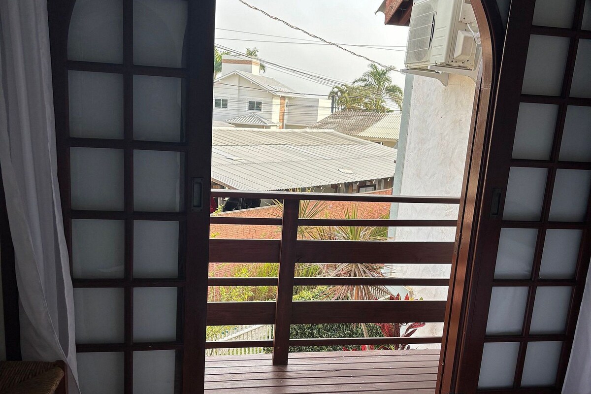 A room with a bed, a chair, and a view through a window with a wooden frame.