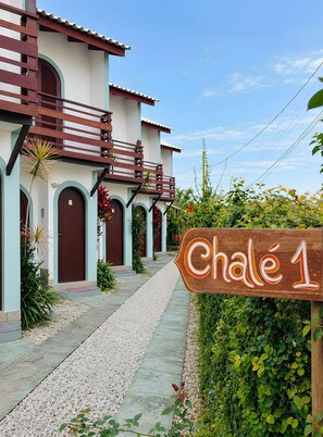 A building with a sign reading 'Chalet 1' in front, featuring a pathway leading to the entrance, surrounded by greenery and a clear sky. - Canto das Borboletas (FlorianĂłpolis)