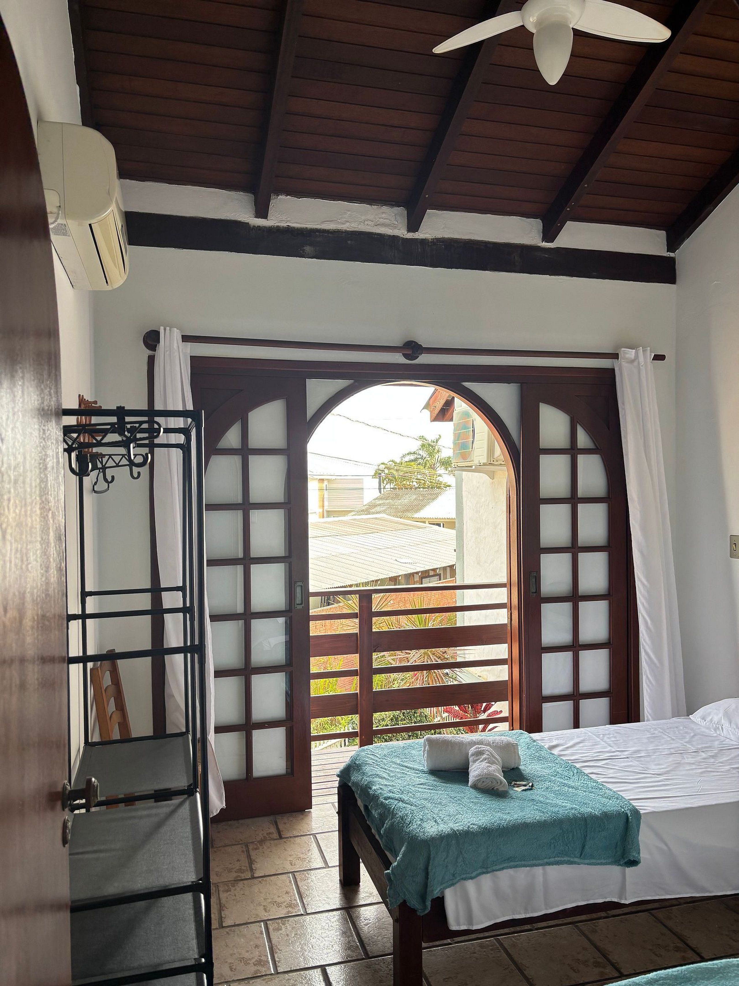 A room with a bed, a ceiling fan, a window with curtains, and a view of the outside.