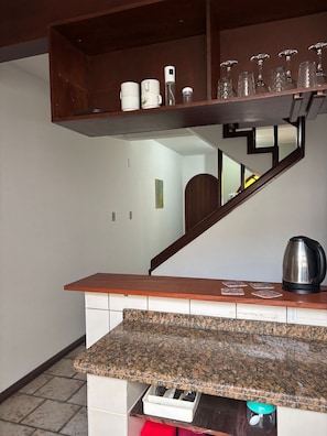 A kitchen with a granite countertop, a coffee maker, a kettle, and a shelf with glassware. - Canto das Borboletas (FlorianĂłpolis)
