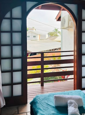 A room with a bed, a wooden railing, and a view of a residential area.