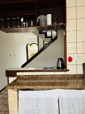 A kitchen with a granite countertop, a coffee maker, and a kettle on a shelf. - Canto das Borboletas (Florianópolis)