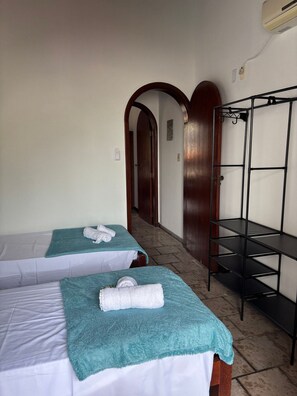 Two single beds with towels, a metal shelf unit, and a hallway leading to a door. - Canto das Borboletas (FlorianĂłpolis)
