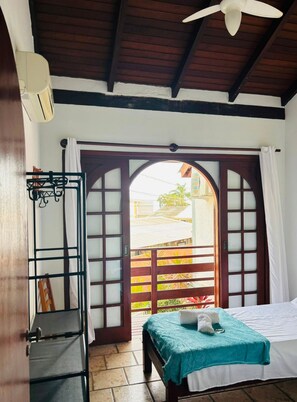 A room with a bed, a ceiling fan, a window with a view, and a door with a metal gate. - Canto das Borboletas (Florianópolis)