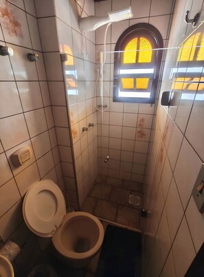 A small, tiled bathroom with a toilet, a shower, and a window.