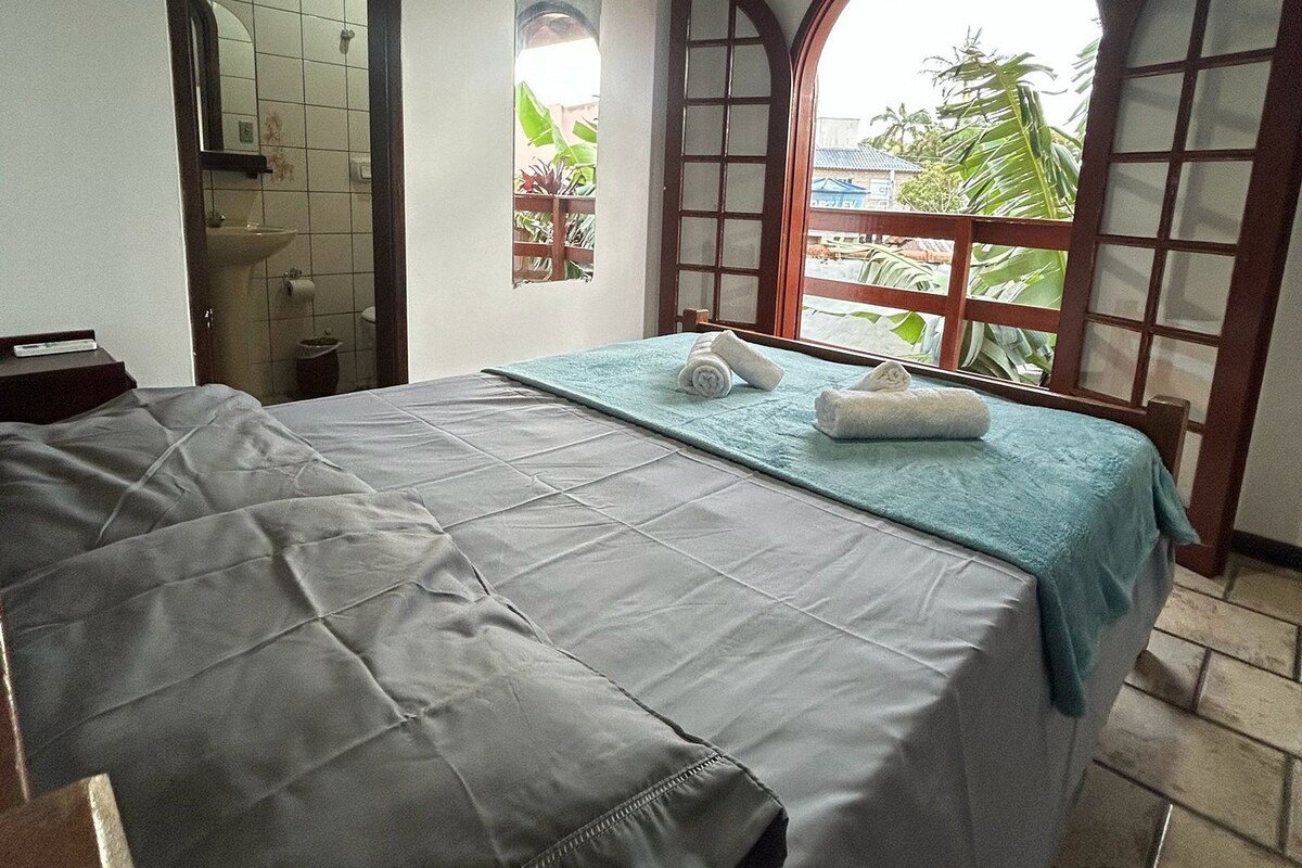 A room with a bed, a window, and a view of greenery outside.