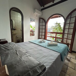 A room with a bed, a window, and a view of greenery outside.