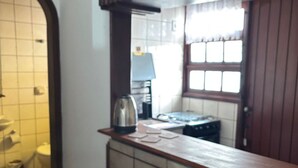 A kitchen with a wooden countertop, two stools, a kettle, and a window with curtains.