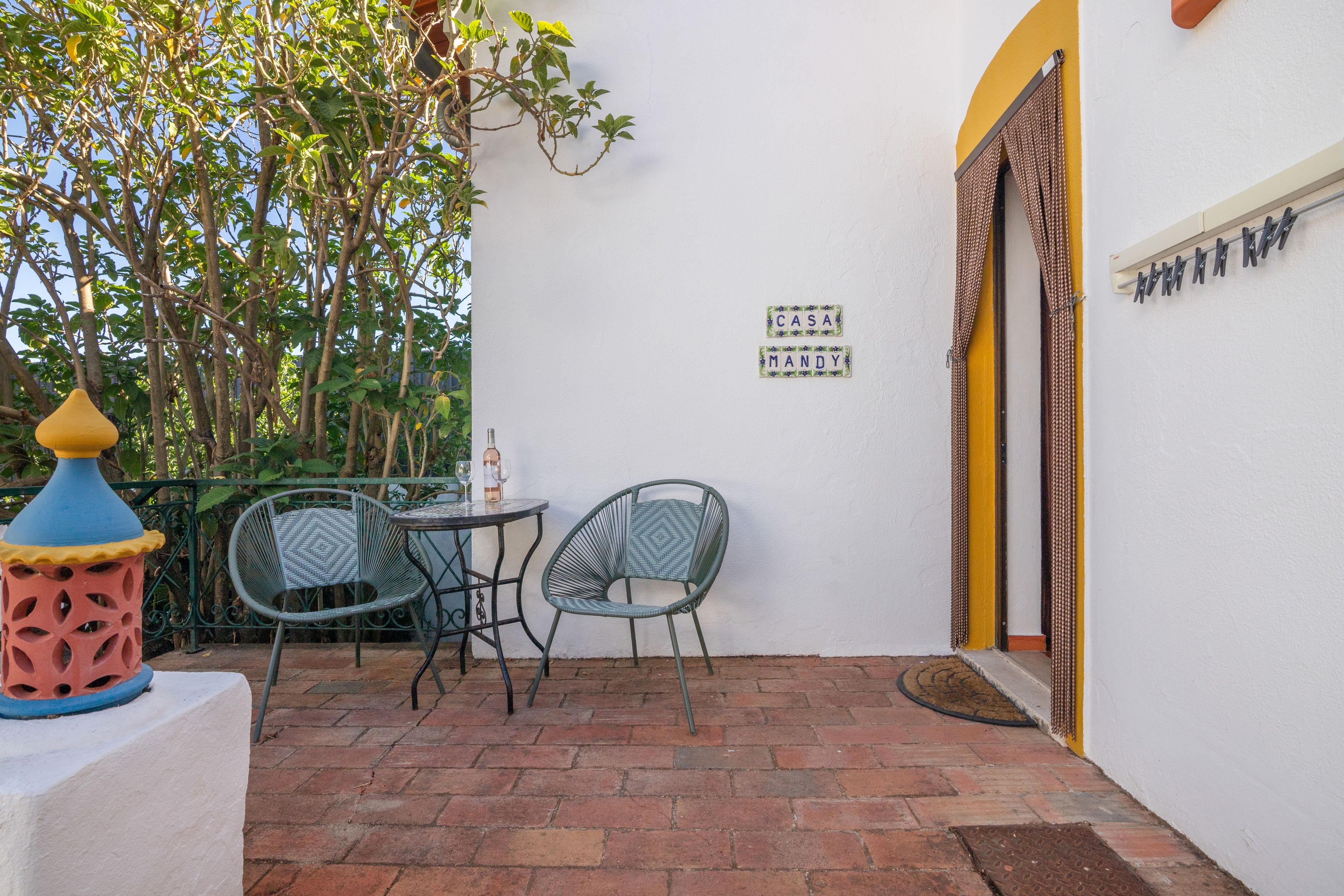 Une terrasse extérieure avec deux chaises et une table, une lampe décorative et un panneau fixé au mur.
