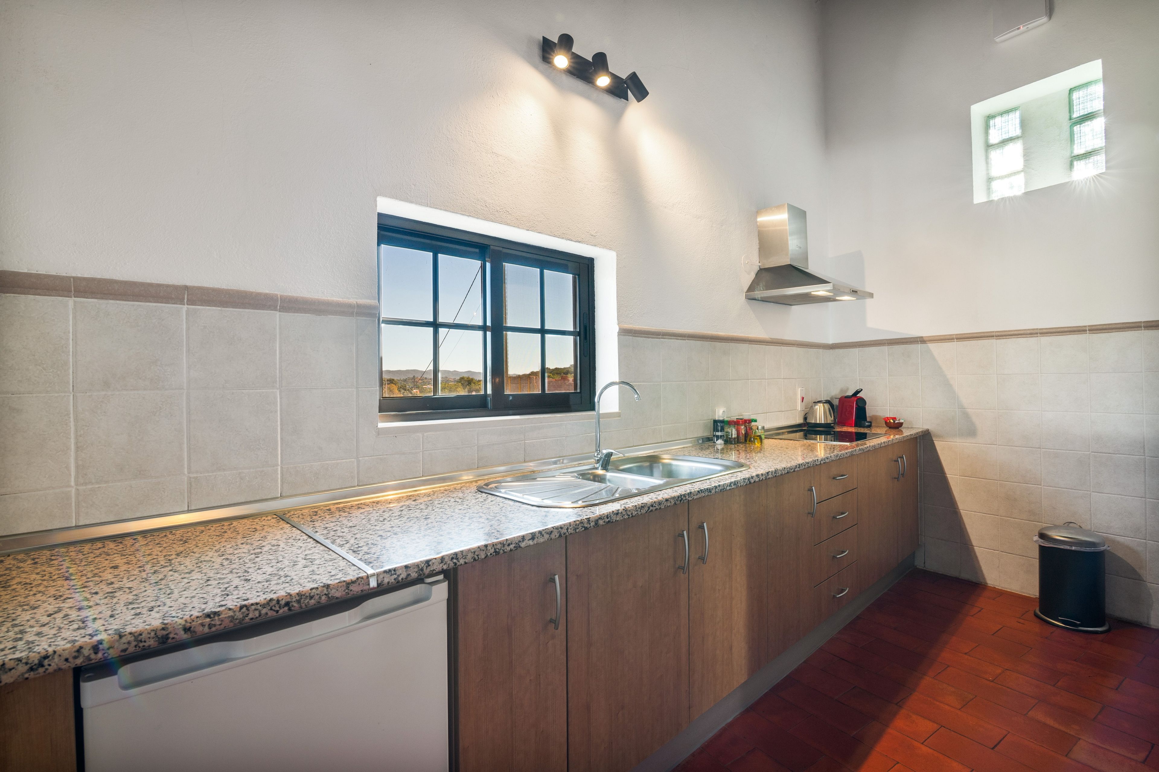 A kitchen with a built-in dishwasher, a stainless steel sink, wooden cabinets, a window with a view, and a range hood.
