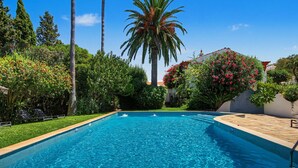 A rectangular swimming pool with clear blue water, surrounded by lush greenery and palm trees.