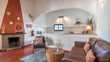 Een gezellige woonkamer met een stenen open haard, een bank, een salontafel en een keukenhoek met een raam.