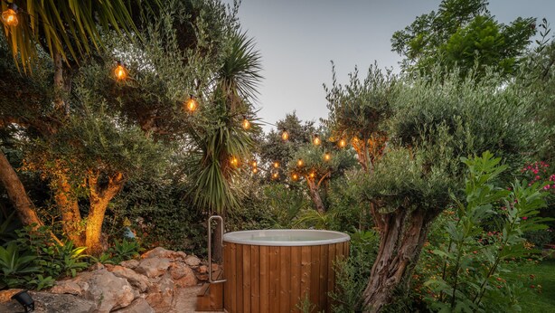 A hot tub surrounded by lush greenery and a stone pathway leading to it.