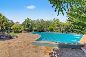 A swimming pool with a tiled edge, surrounded by lounge chairs and umbrellas, set in a landscaped garden with various plants and trees. - Holiday Home 'Ferrobo - Casa Mandy' with Shared Pool, Wi-Fi and Air Conditioning (Farrobo)