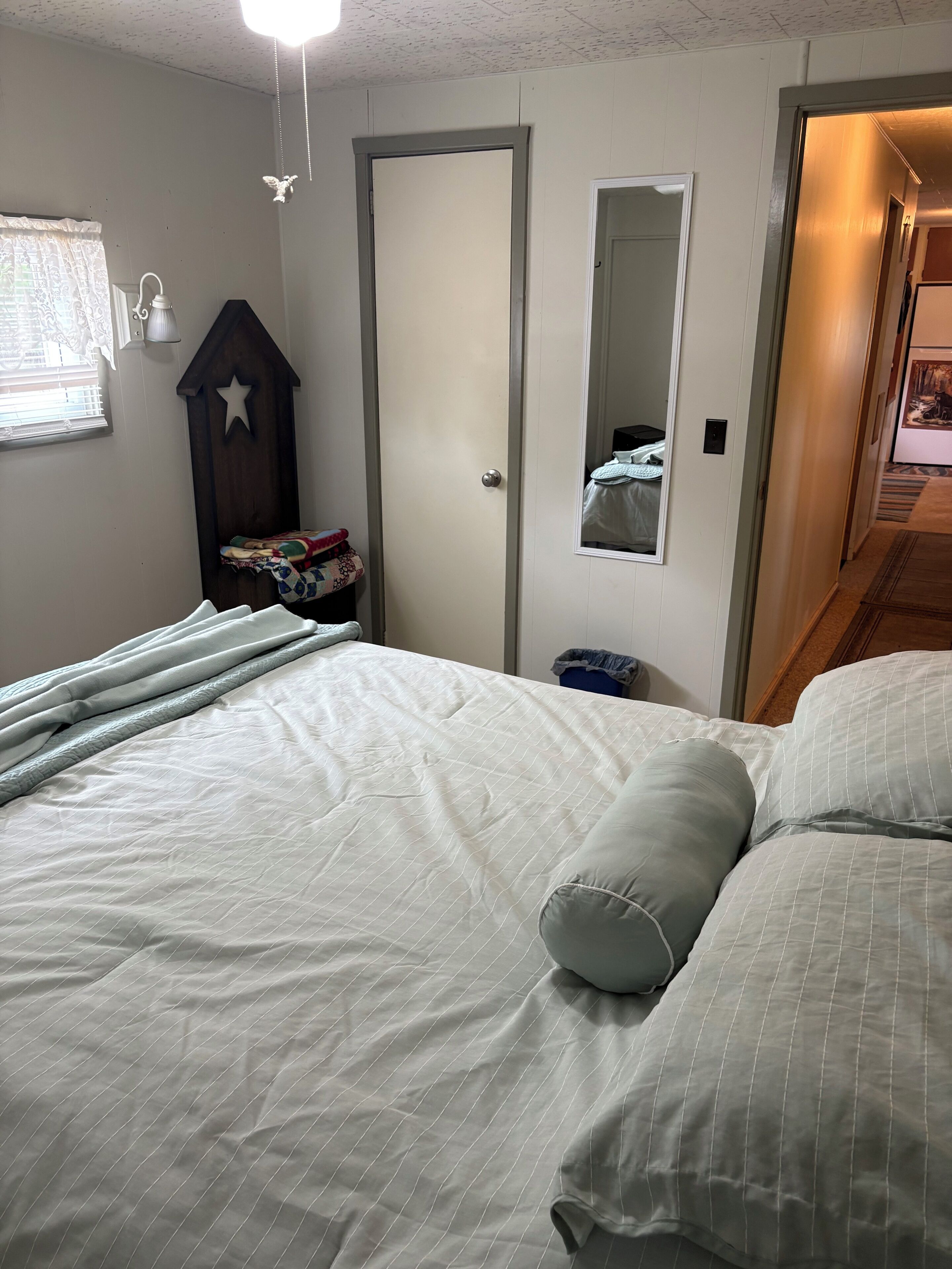 Una camera da letto con un letto, un comodino, una cassettiera, uno specchio e una porta.