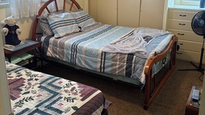 Une chambre à coucher comprenant un lit, une table de chevet, une commode, un ventilateur de plafond et une fenêtre avec des rideaux.