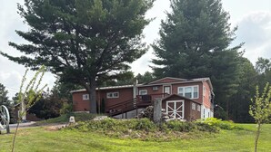 Une maison à deux étages avec une façade rouge, une terrasse en bois et un mur en pierre.