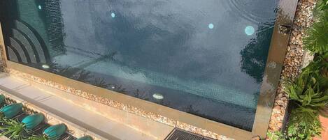 A swimming pool with a clear view of the water, surrounded by a pebble border and a small statue.