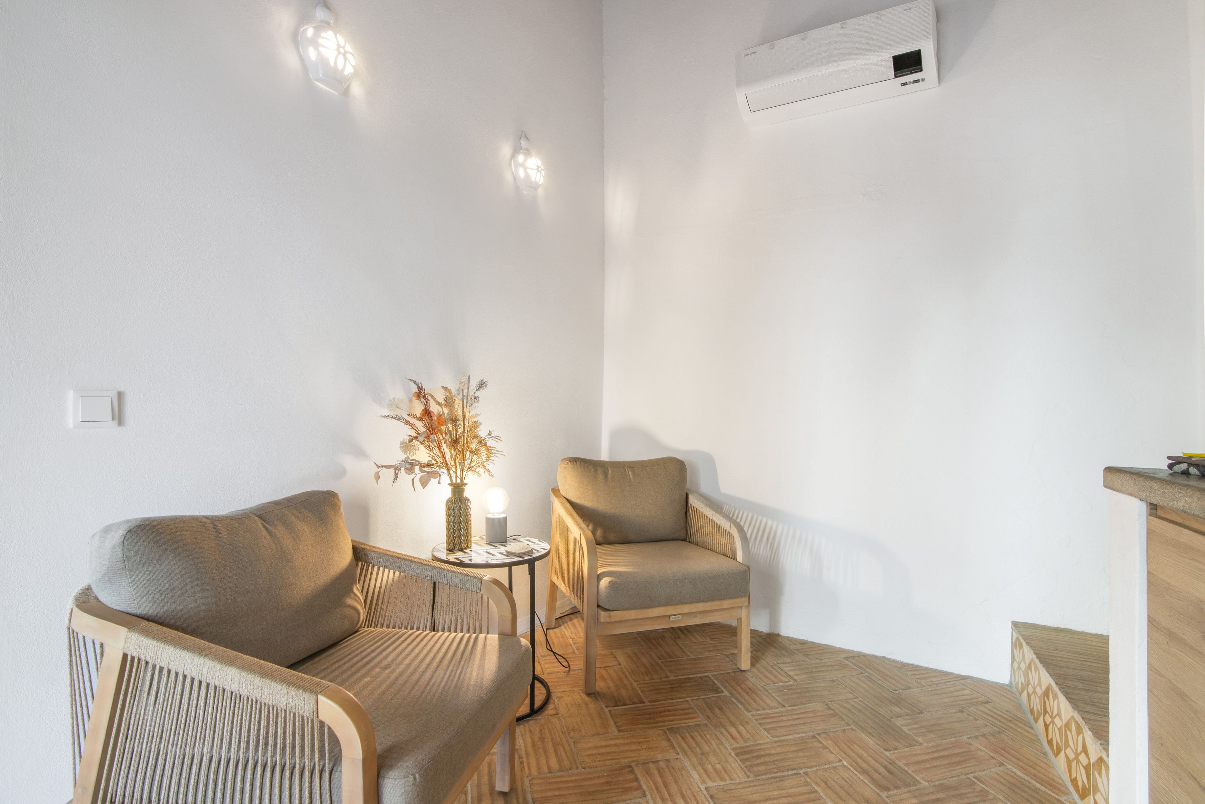 A small, well-lit room with two armchairs, a small table with a vase and candle, and a radiator.
