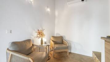 A small, well-lit room with two armchairs, a small table with a vase and candle, and a radiator.