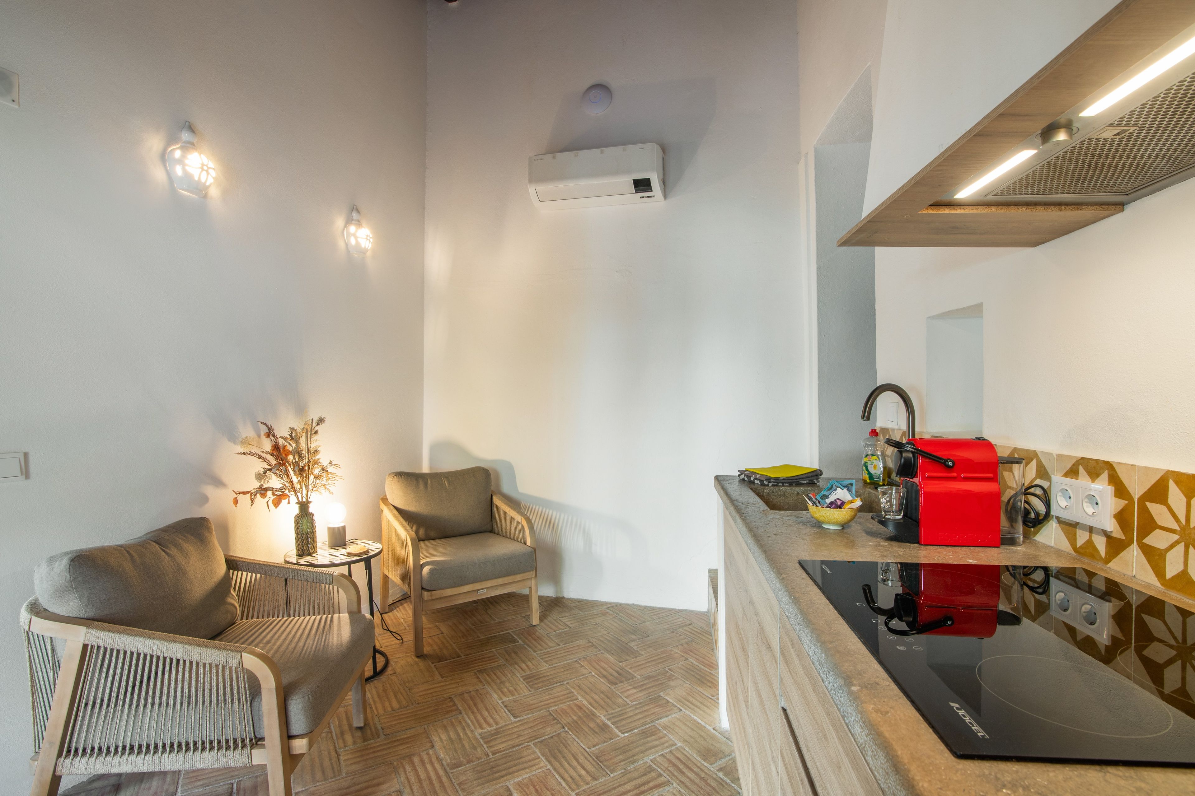 Un espace de vie compact comprenant un coin cuisine, un coin repas avec deux chaises, une petite table et un vase décoratif.