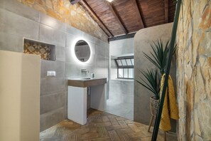 Une salle de bain avec un mur en pierre, un miroir rond, un lavabo et une plante en pot.