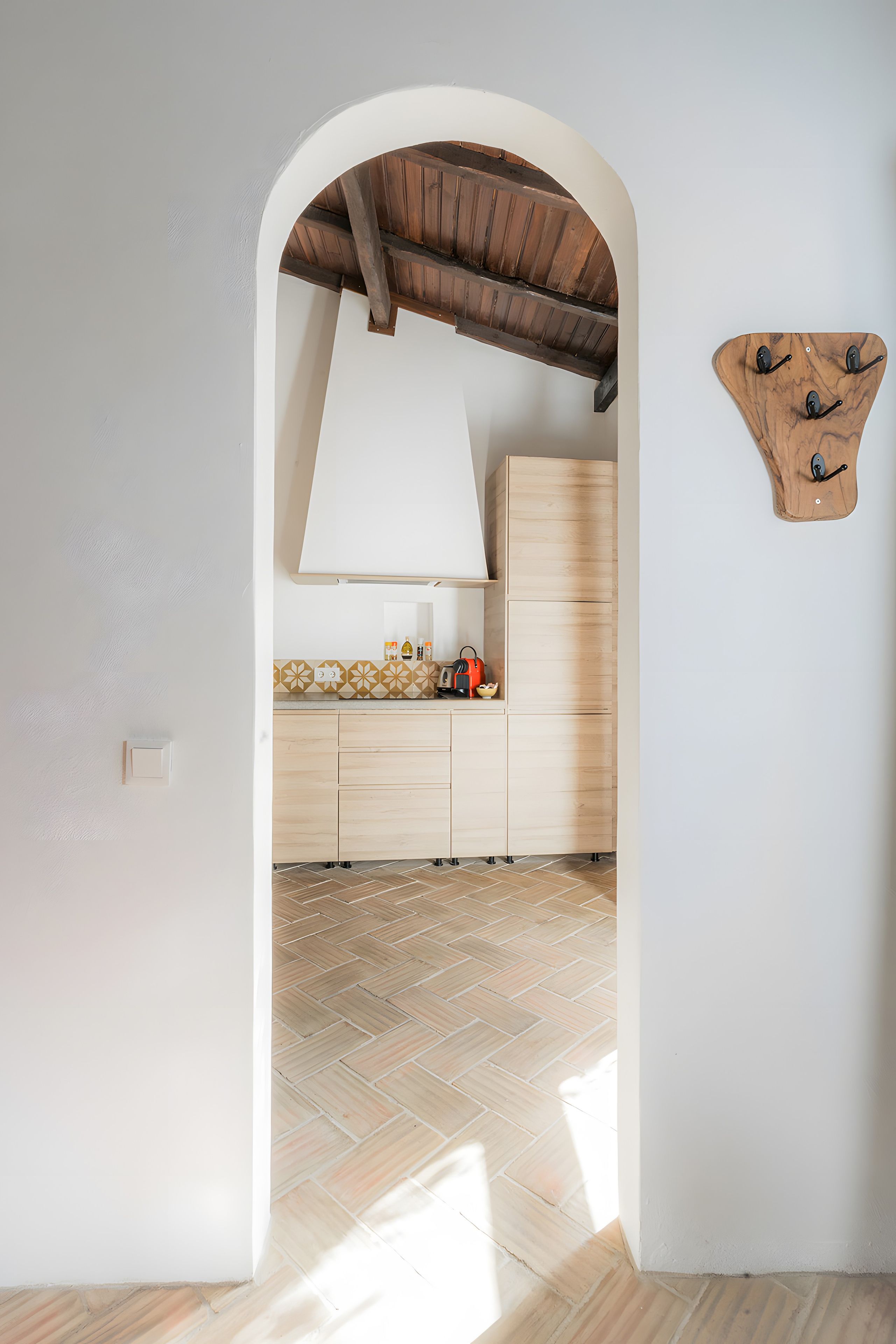 Une cuisine avec une arche blanche donnant sur un coin repas, des meubles en bois et un luminaire fixé au mur.