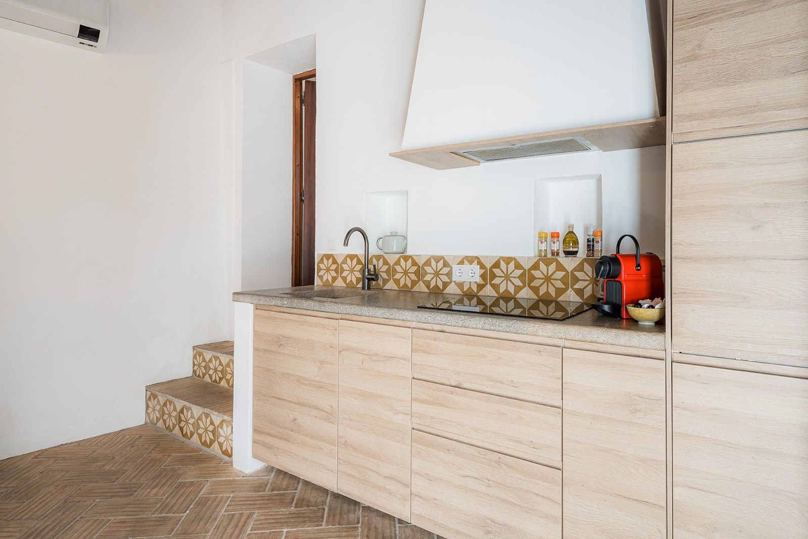 Une cuisine avec un sol à motifs en chevrons, un plan de travail agrémenté d’un pare-feu géométrique et un appareil électroménager rouge.
