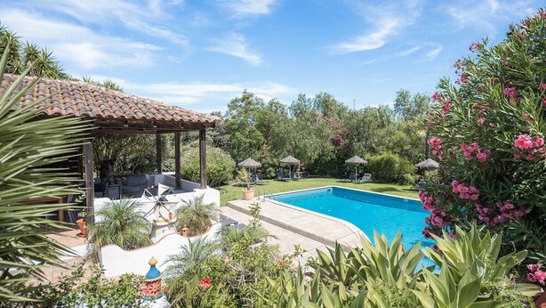 A swimming pool with a pergola and lounge chairs, surrounded by lush greenery and flowering plants. - Holiday Home 'Casa Ferrobo - Amy' with Shared Pool, Wi-Fi and Air Conditioning (Farrobo)