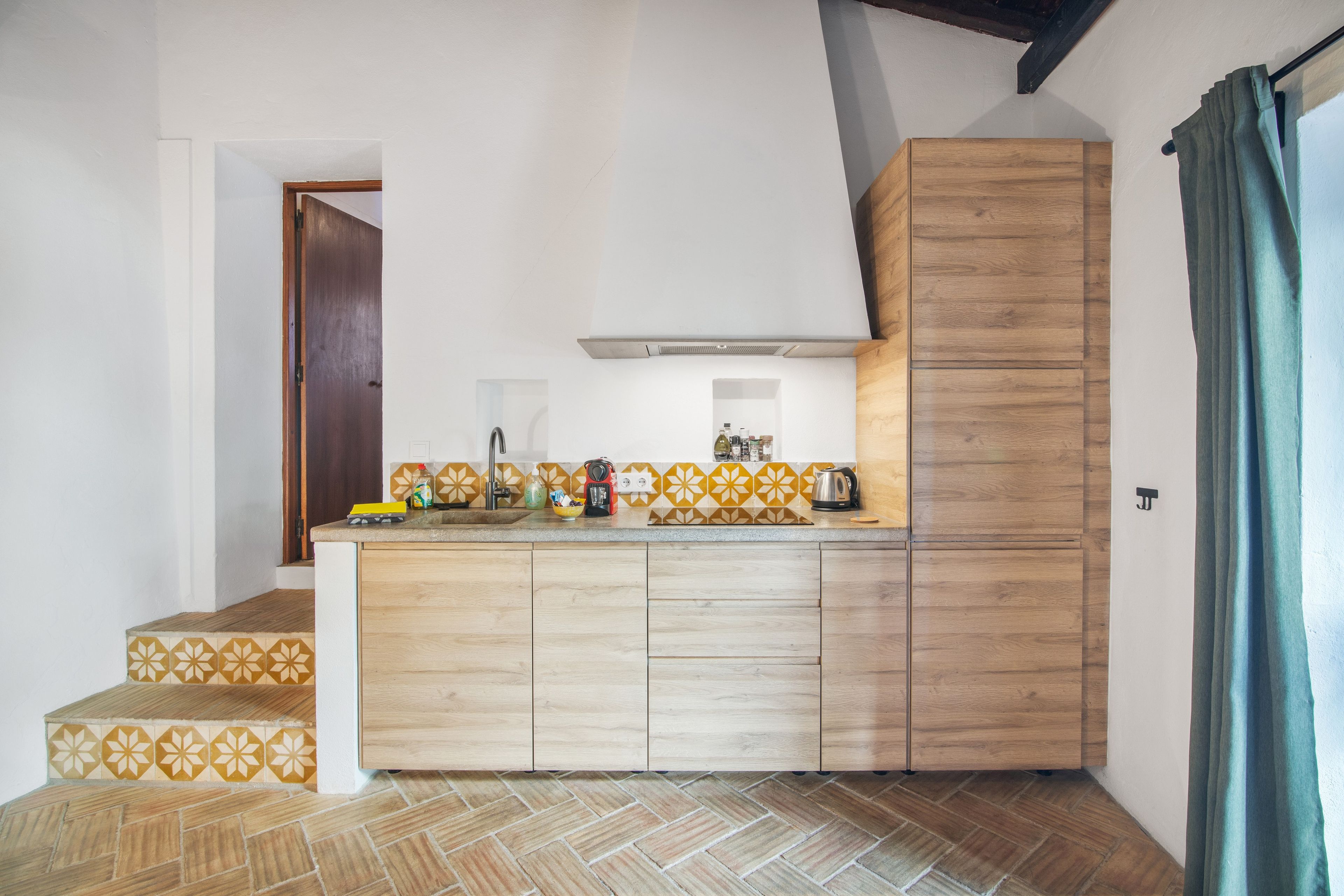 A compact kitchen with a wooden cabinet, a sink, and a herringbone-patterned floor.
