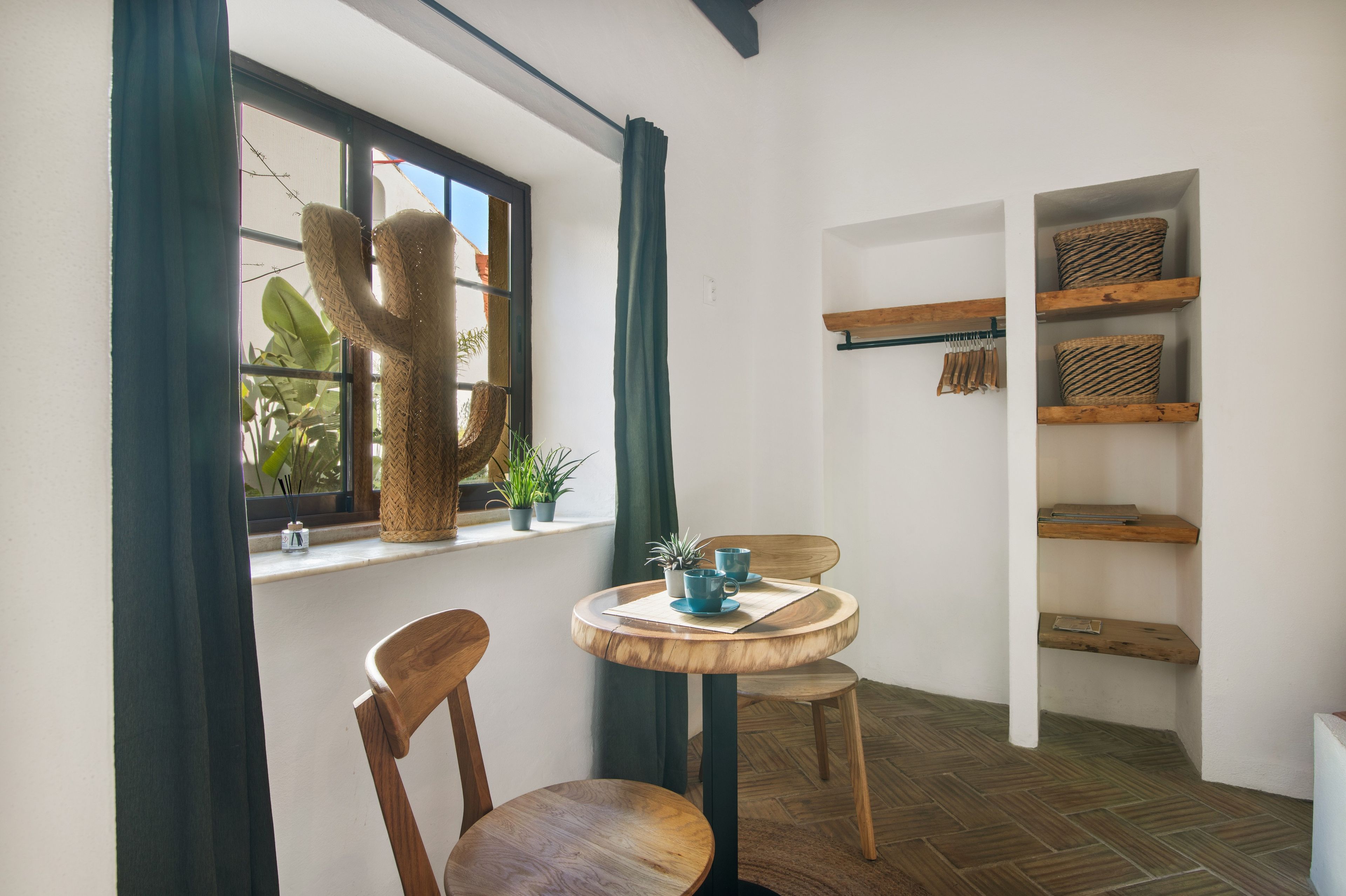 A room with a round wooden table, two chairs, a cactus sculpture, and shelves with baskets.
