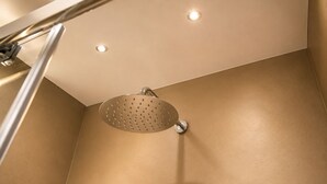 Un cabezal de ducha con diseño circular y acabado metálico, instalado en una pared de superficie color beige.