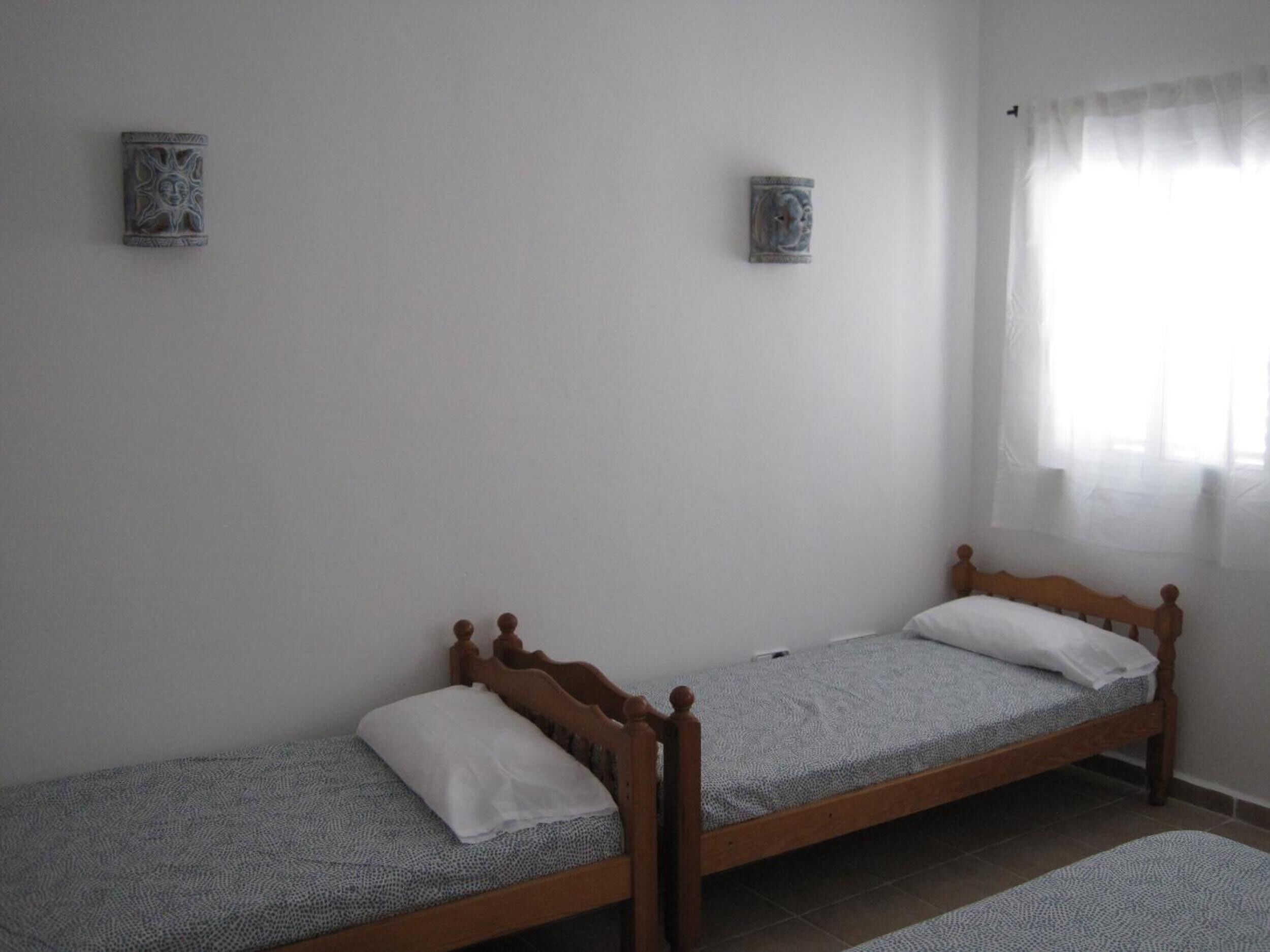 Una habitación con dos camas individuales, una ventana con cortinas traslúcidas y dos adornos en la pared.