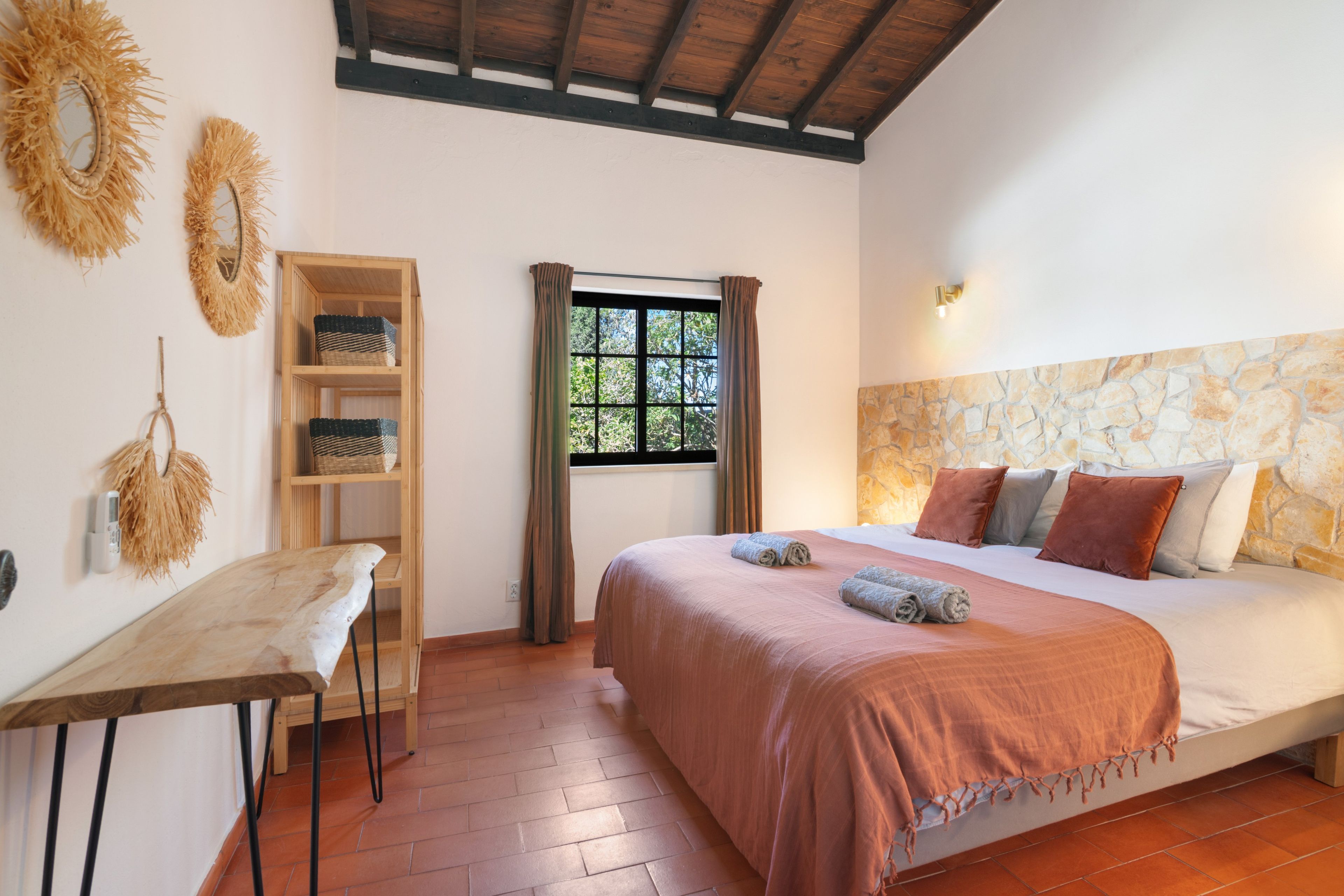 A bedroom with a bed, a wooden desk, a window with curtains, and wall-mounted baskets.