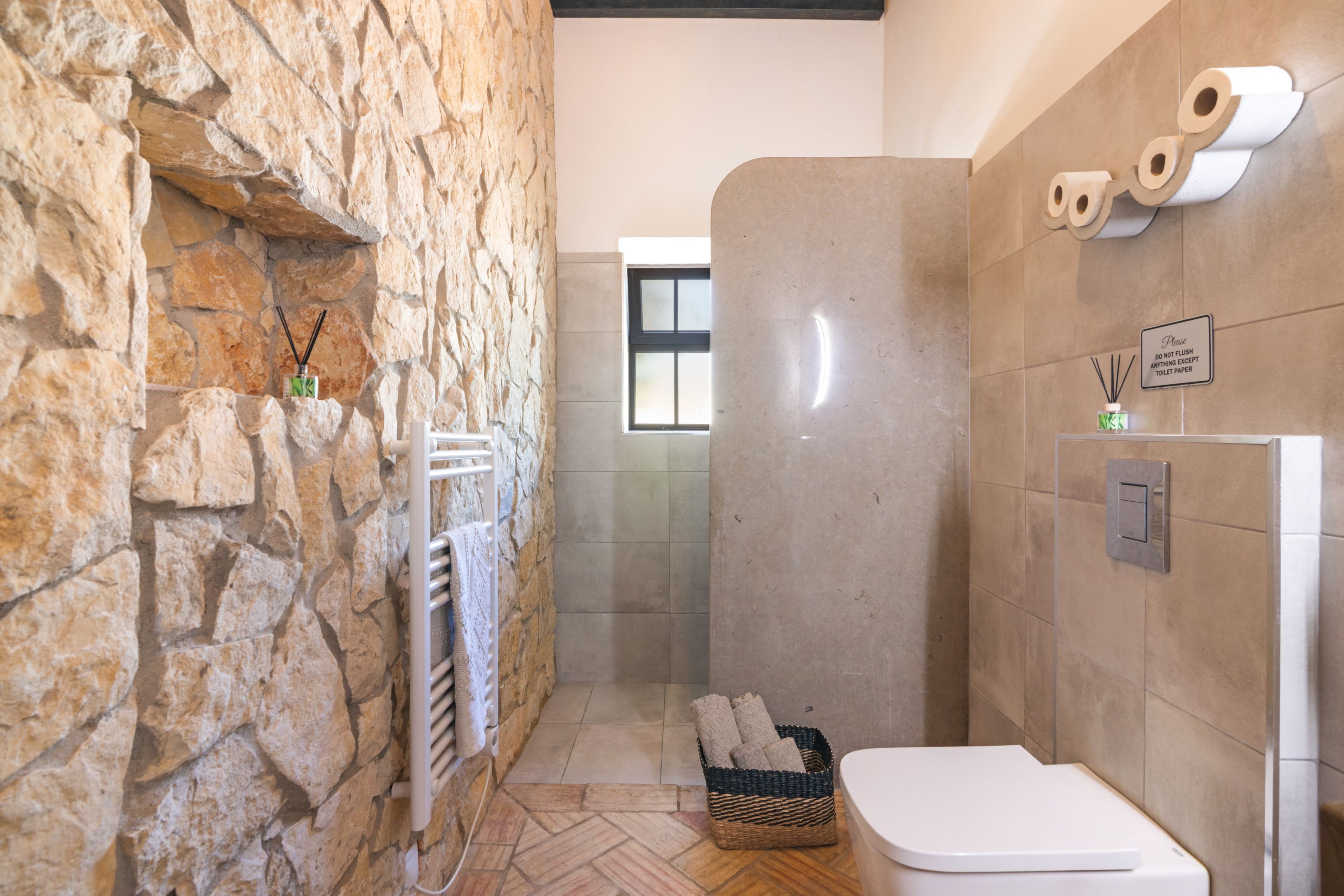 A bathroom with a stone wall, a white toilet, a shower area, and a basket with towels.