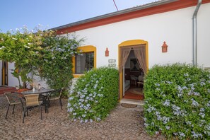 Ein Innenhof mit Tisch und Stühlen, einer überdachten Sitzgelegenheit und einem Gebäudeeingang.
