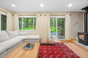 A modern living room with a sofa, a coffee table with a book, a red patterned rug, and a fireplace. - A-Frame Retreat - Hot Tub, Fire Pit & Fireplace (Monroe County)