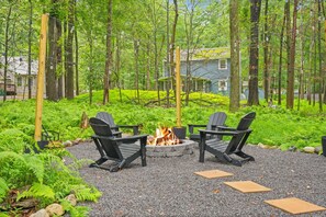 An outdoor seating area with two Adirondack chairs around a fire pit, surrounded by a forested area. - A-Frame Retreat - Hot Tub, Fire Pit & Fireplace (Monroe County)