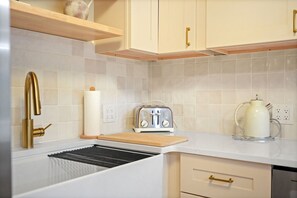 A kitchen with white cabinets, a gold faucet, a toaster, and a kettle on the counter. - A-Frame Retreat - Hot Tub, Fire Pit & Fireplace (Monroe County)