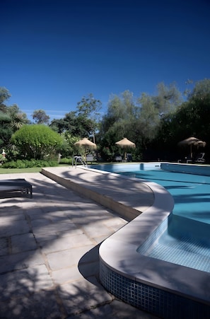 A swimming pool with a curved edge, surrounded by greenery and shaded by trees. - Holiday Home 'Casa Ferrobo - Gemma' with Shared Pool, Wi-Fi and Air Conditioning (Farrobo)