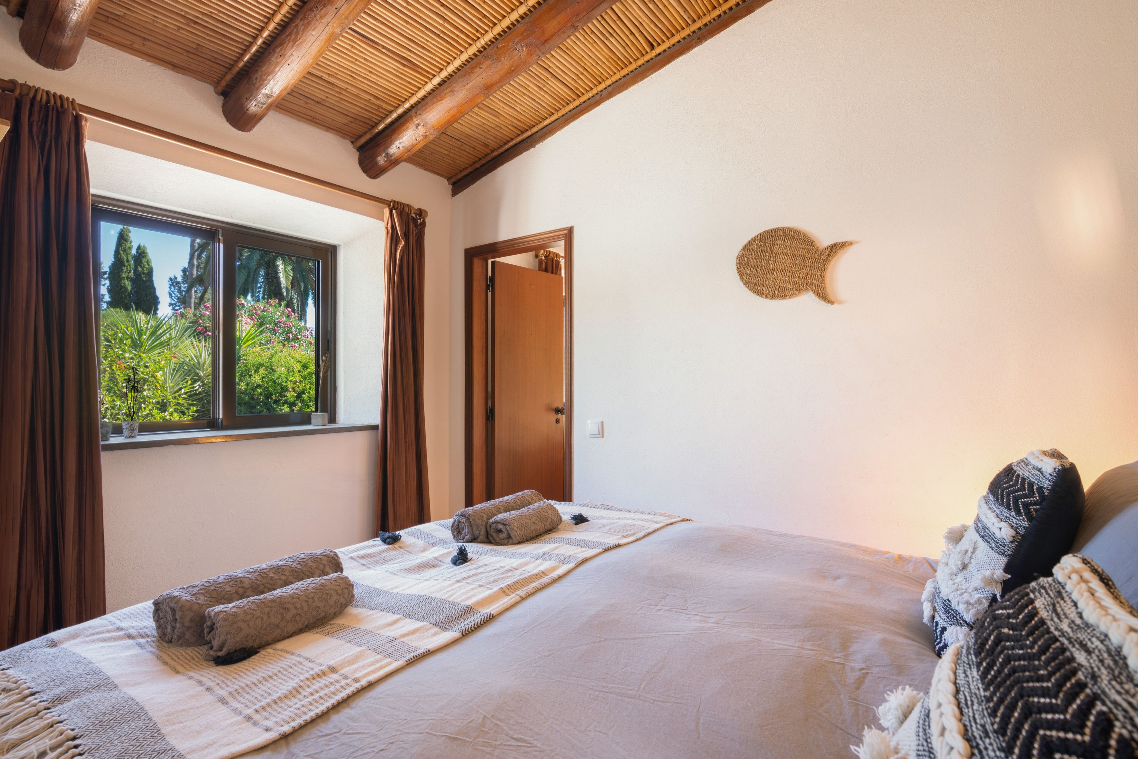 A bedroom with a large bed, a window with curtains, a door, and a wall decoration.
