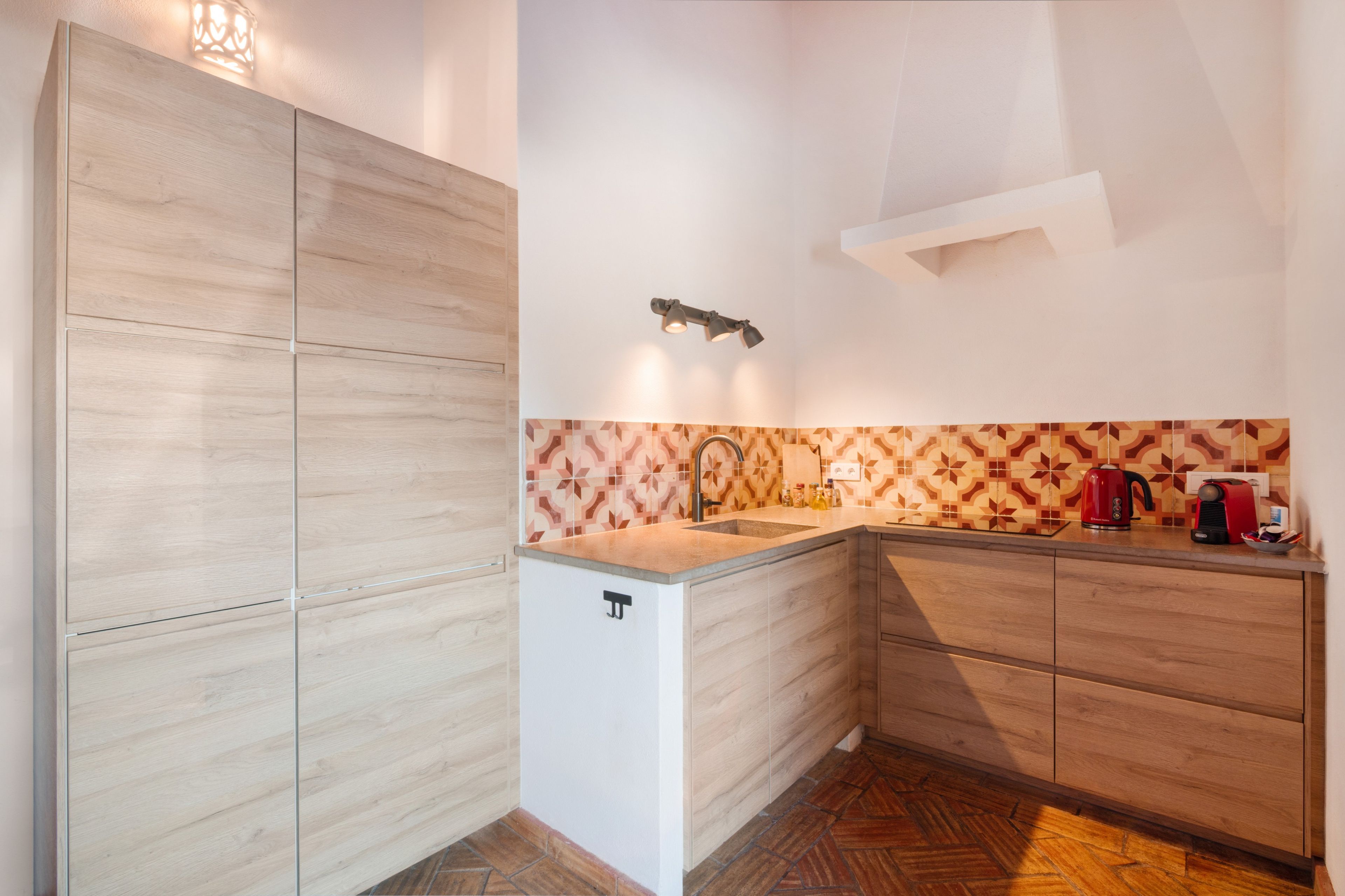 Une cuisine moderne avec des meubles en bois, un réfrigérateur blanc, un crédence à motifs et une bouilloire rouge.