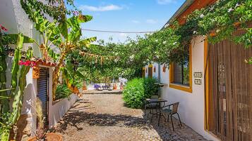 Une ruelle étroite pavée de pierres, avec un espace patio aménagé avec des sièges en plein air et un pot de fleurs.